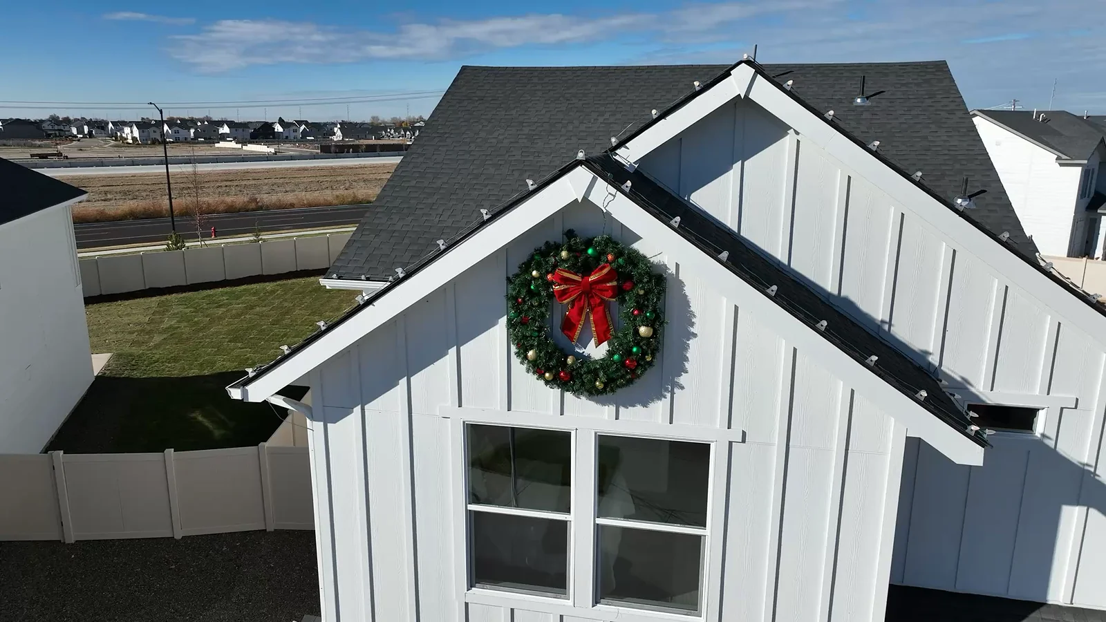 White board-and-batten CBH model home with a large holiday wreath and roofline lights